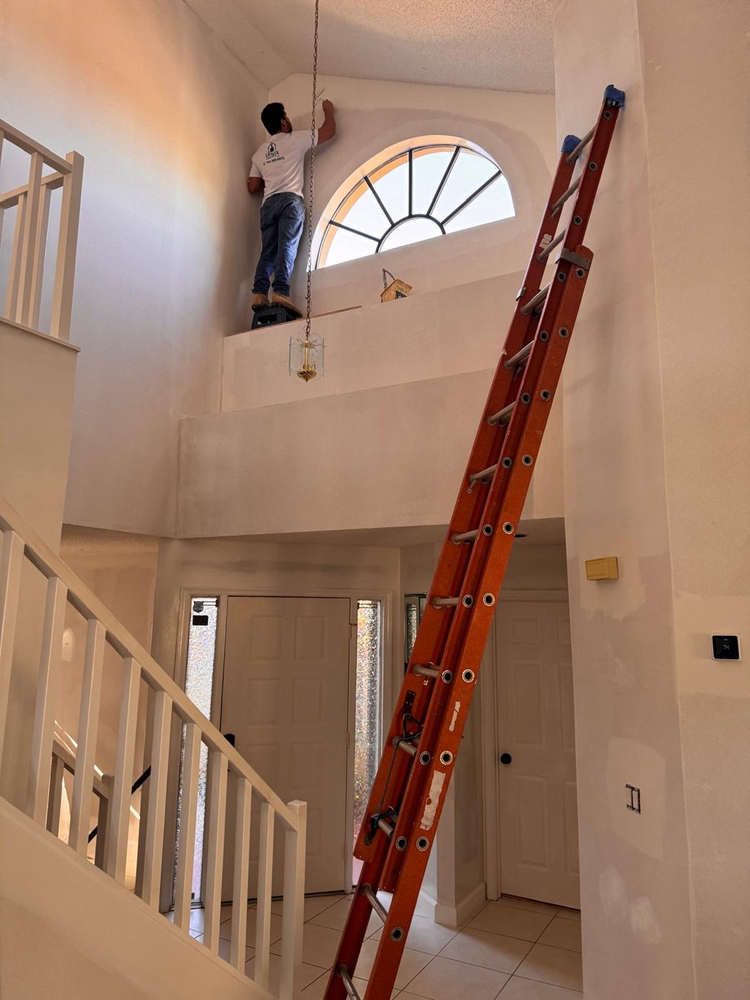 Lenix Home Services technician painting a high entryway wall
